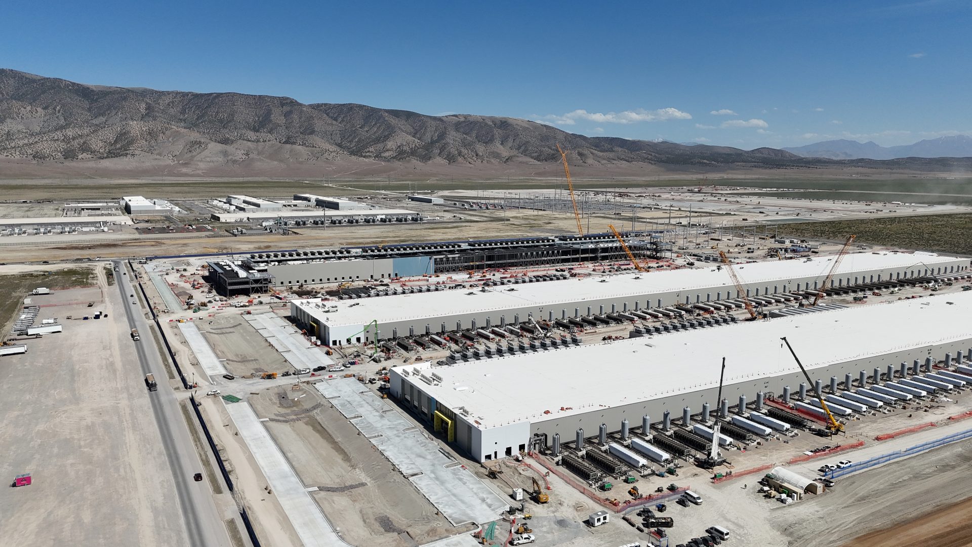 An aerial view of three extremely large buildings under construction. They are surrounded by cranes, trucks, and other construction equipment. People are too small to be visible - large trucks are barely visible.