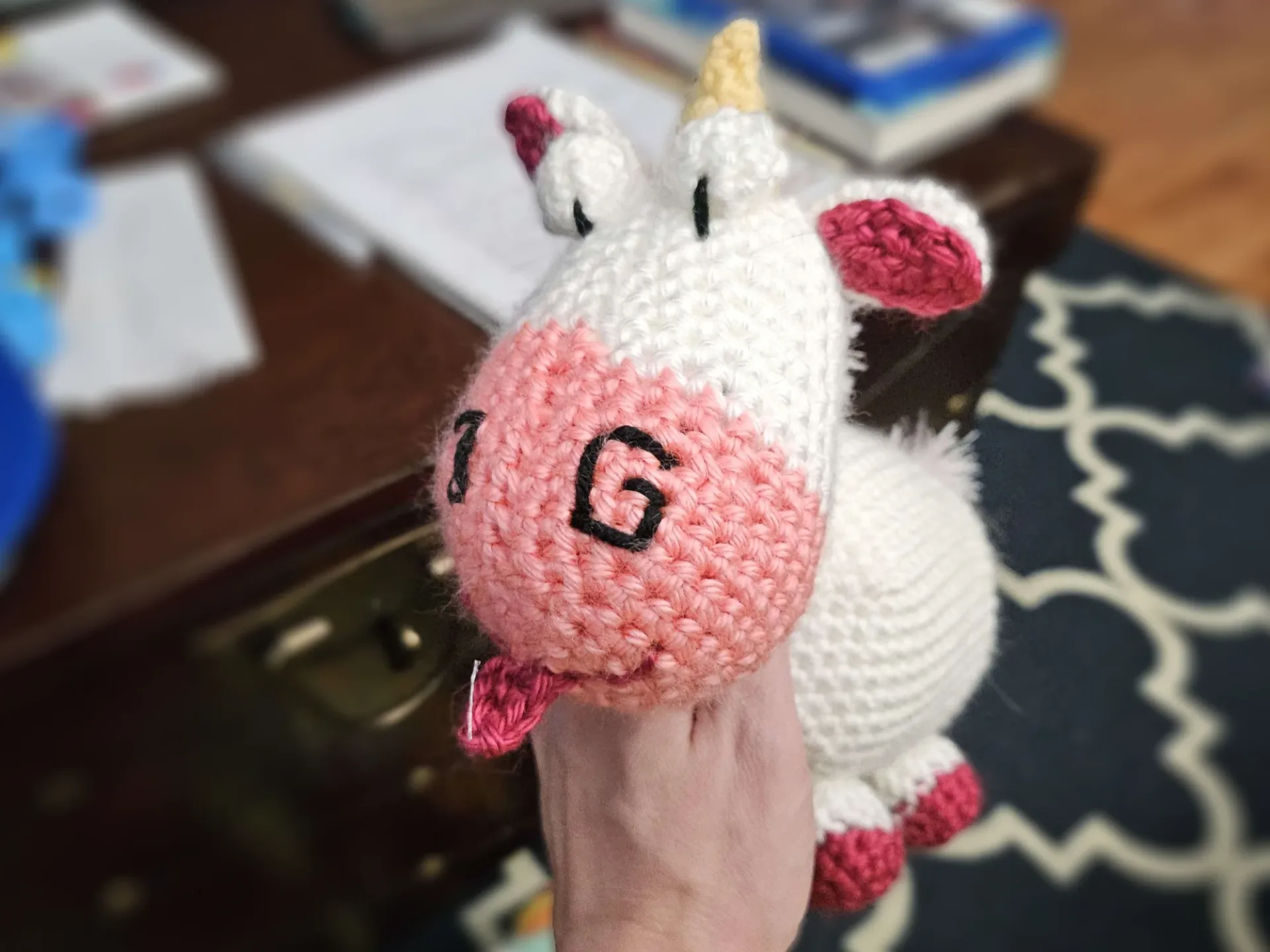 A crocheted unicorn facing front with bulging eyes and a silly tongue-out smile.
