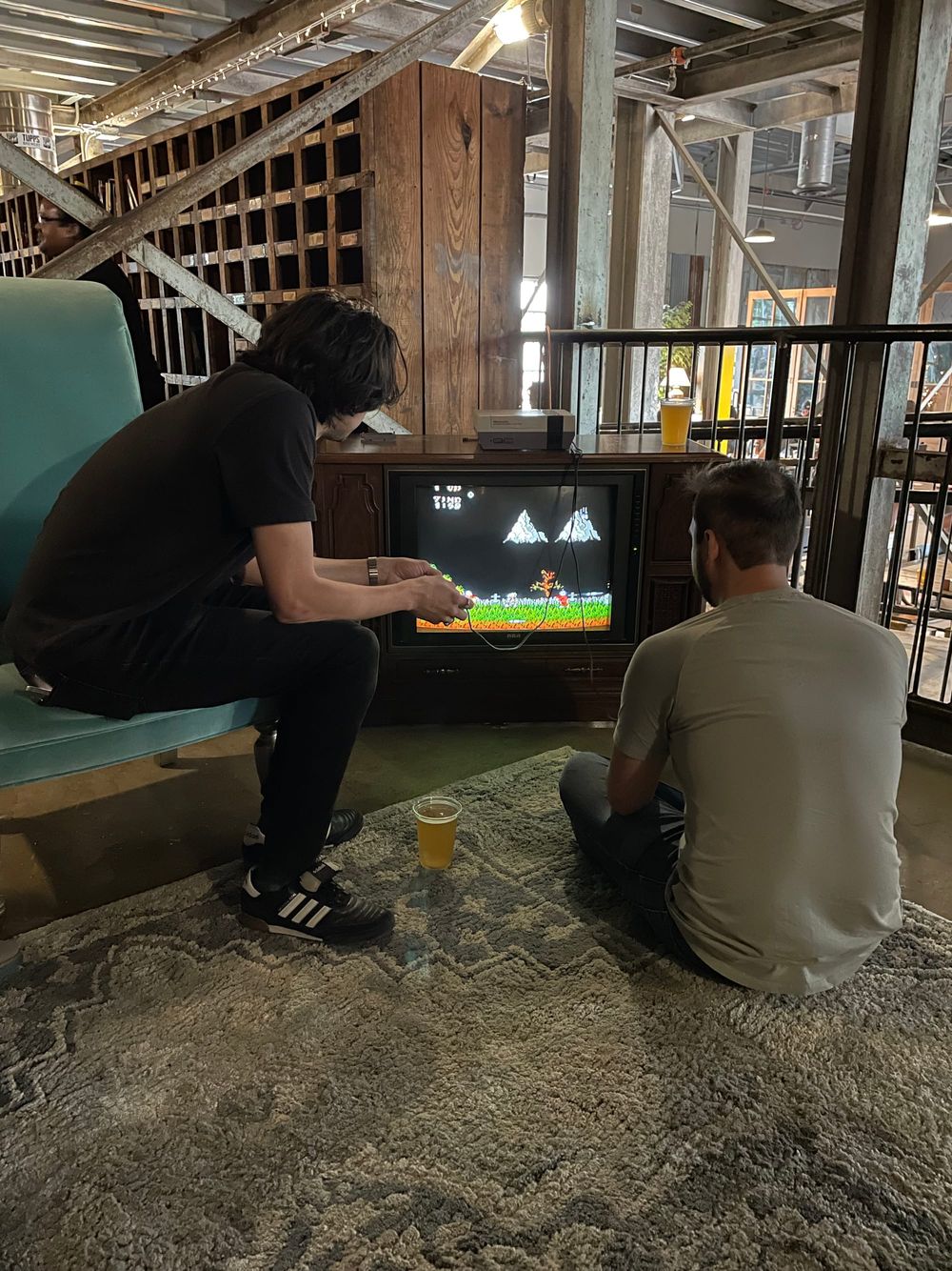 Two guys, one sitting in a couch and another in the floor, playing video games in an old TV