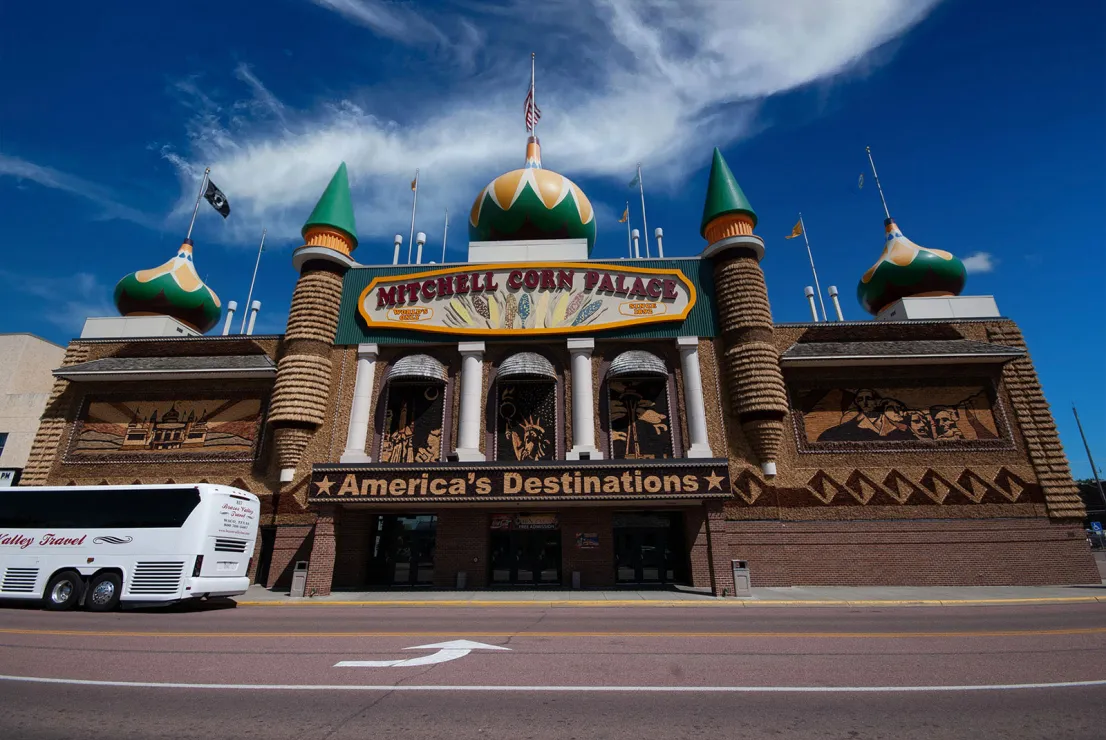 A palatial building with turrets that look very Russian in design sits under a blue, blue sky. The marquees at the front of the building read "Mitchell Corn Palace" and "America's Destinations," and there's a tour bus parked in front, right near the main entrance.