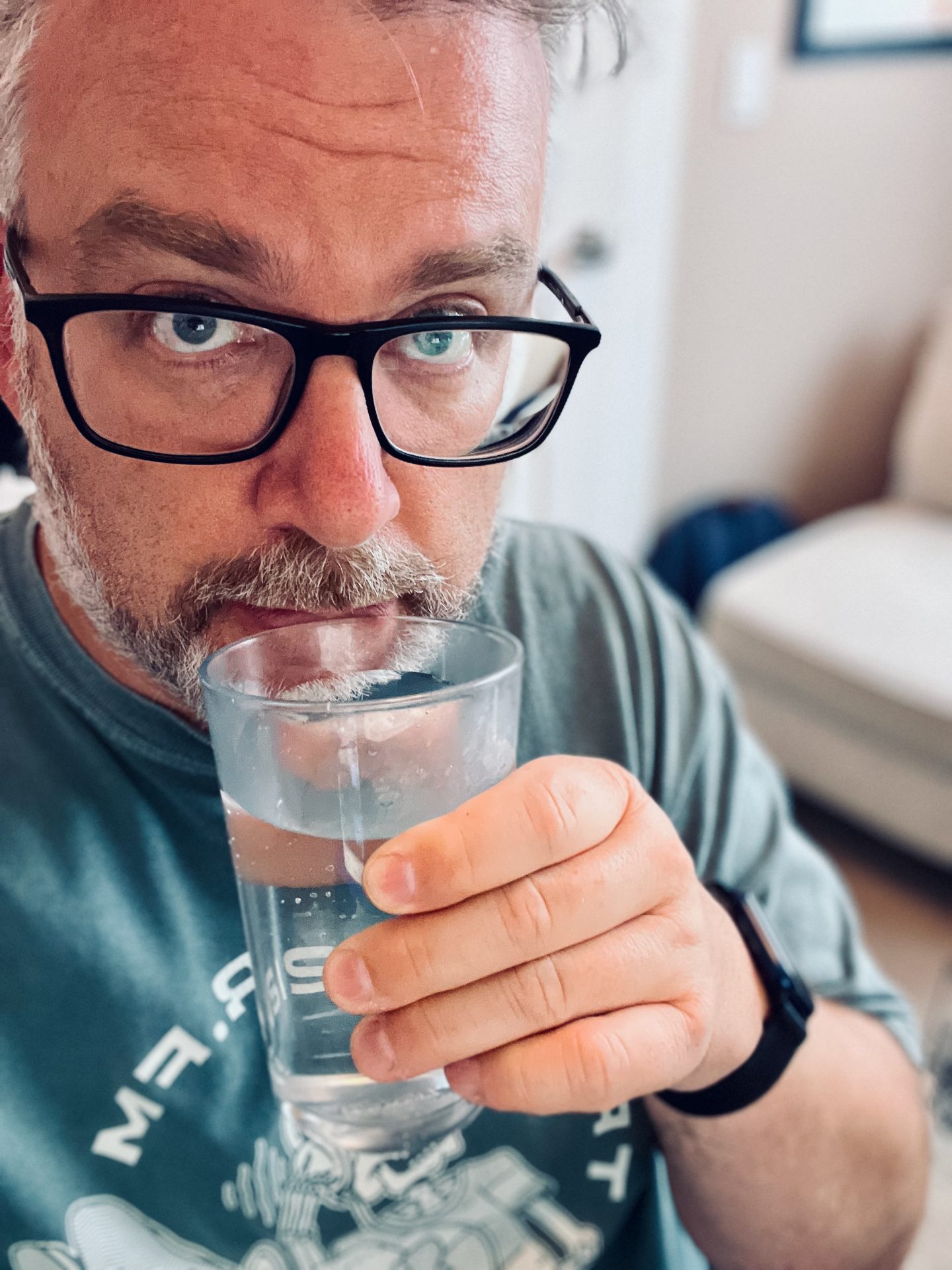 Photo of me, a adult white male with glasses and a beard wearing a Transistor.fm t shirt drinking a glass of water.
