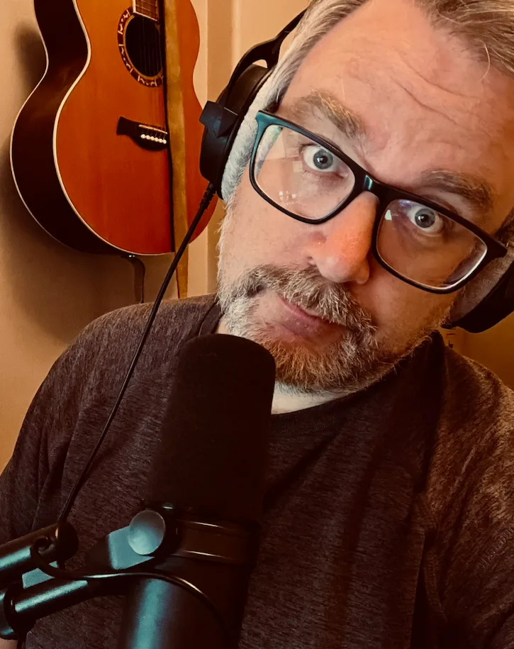 Selfie of me with a microphone in the foreground and a acoustic guitar in the background.