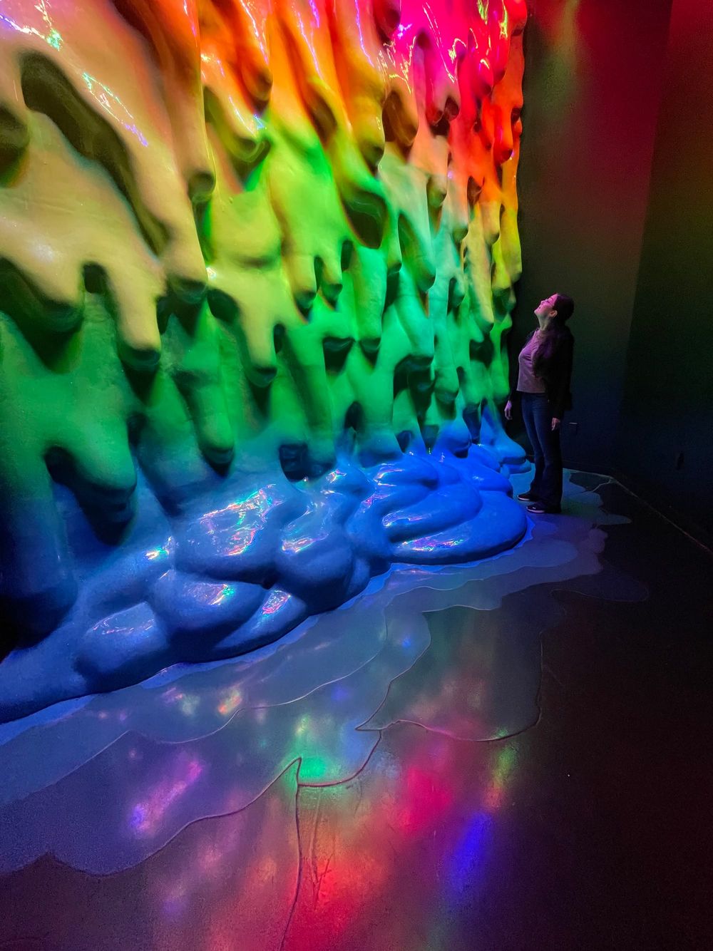Rainbow colored tall wall with a goomy texture and a person looking up high