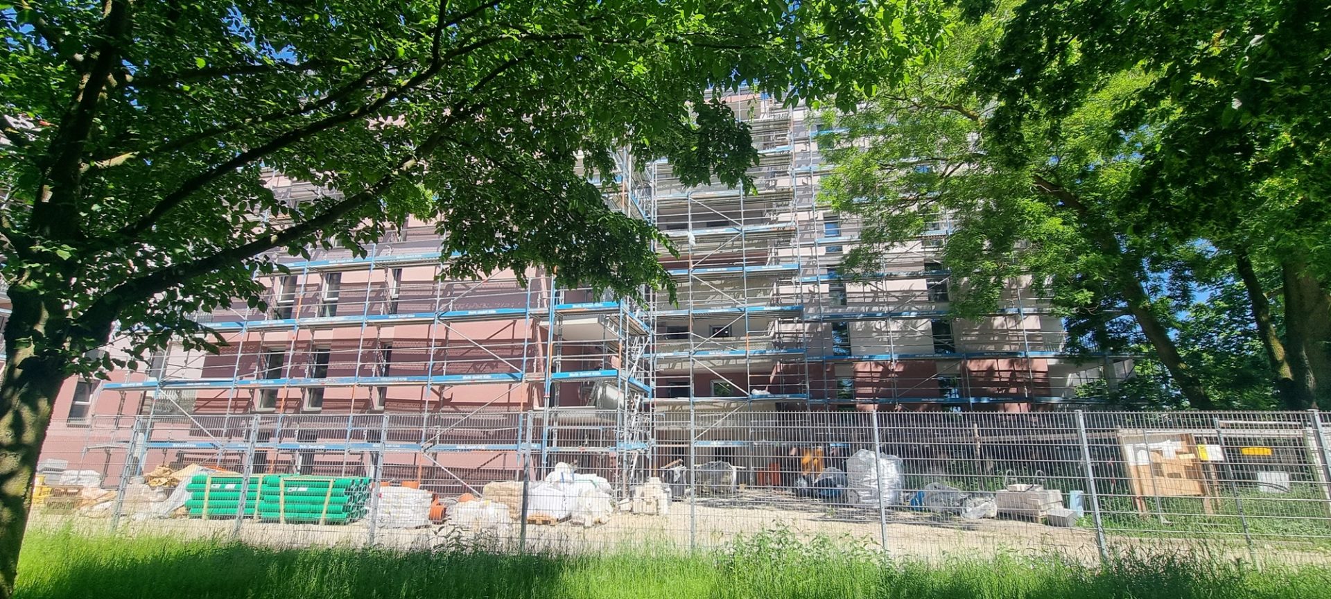 Einergerüsteter Neubau eines Mehrparteienhaus. Teilweise durch einen Baum verdeckt.
