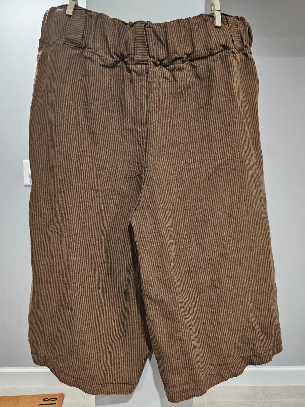 Rumpled linen pants hang on a wall.