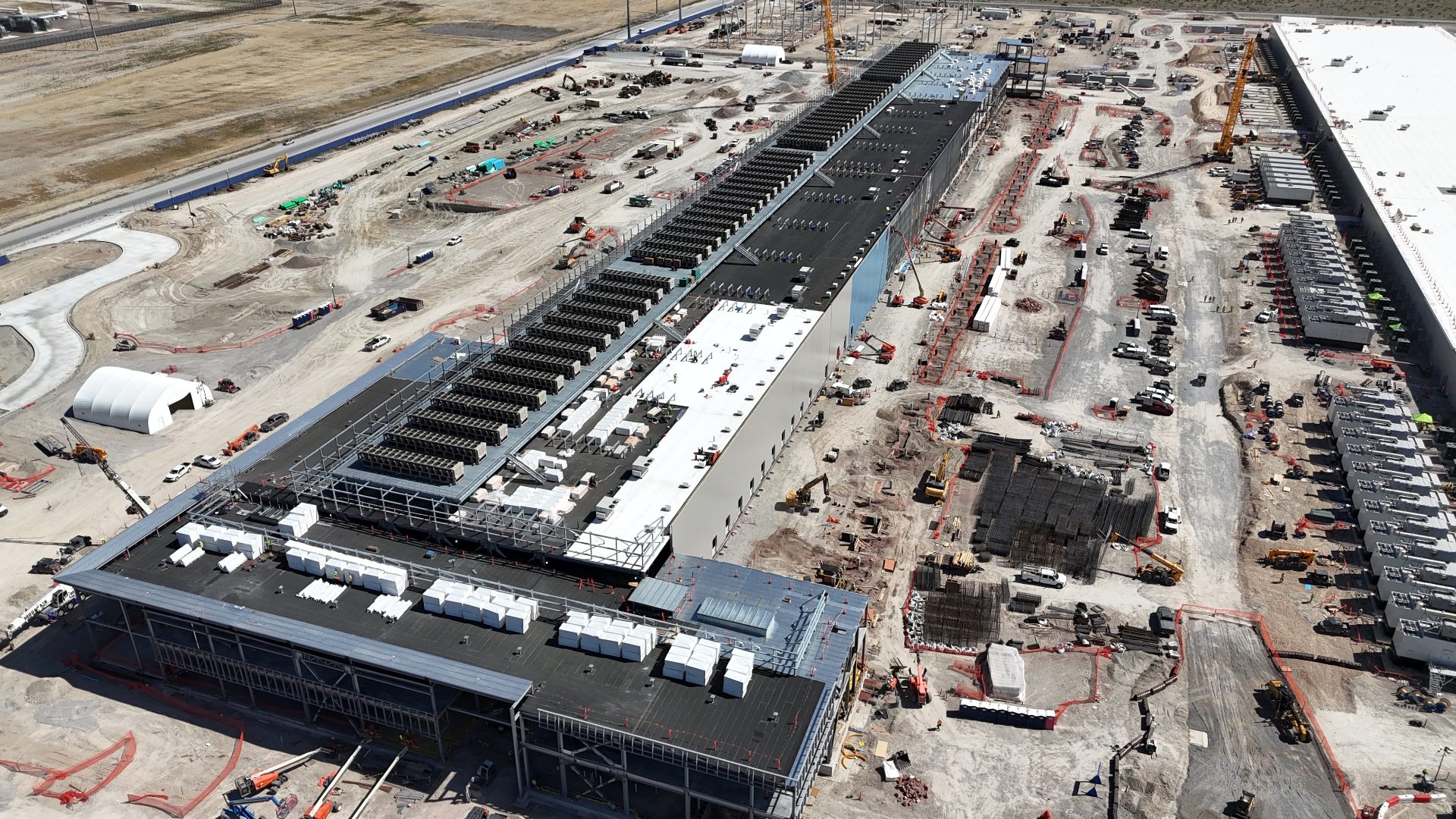 An aerial view of three extremely large buildings under construction. They are surrounded by cranes, trucks, and other construction equipment. People are too small to be visible - large trucks are barely visible.