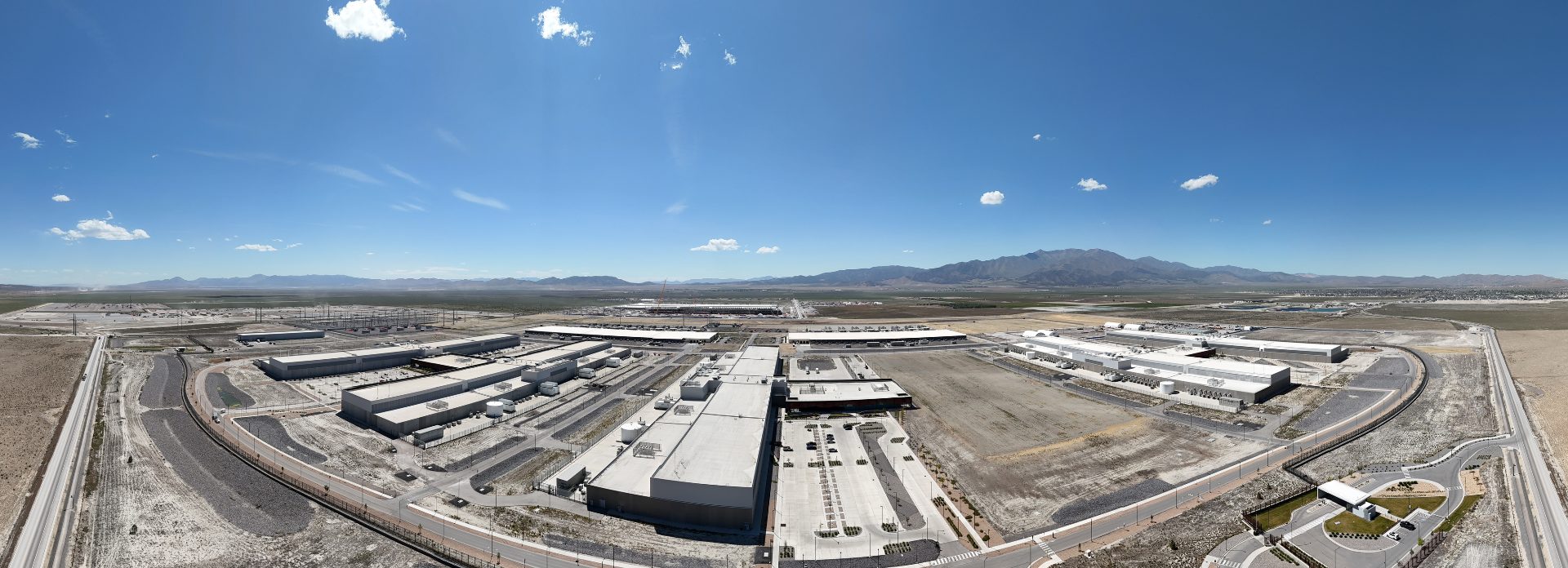 A massive campus stretches out into the distance. In the foreground, two large, long buildings can be seen, surrounded by generation and cooling equipment. The whole campus is ringed by a road.