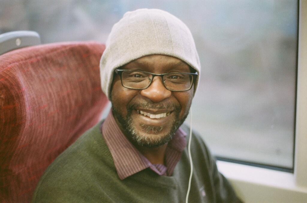 A smiling man wearing glasses and a hat that I met on a train