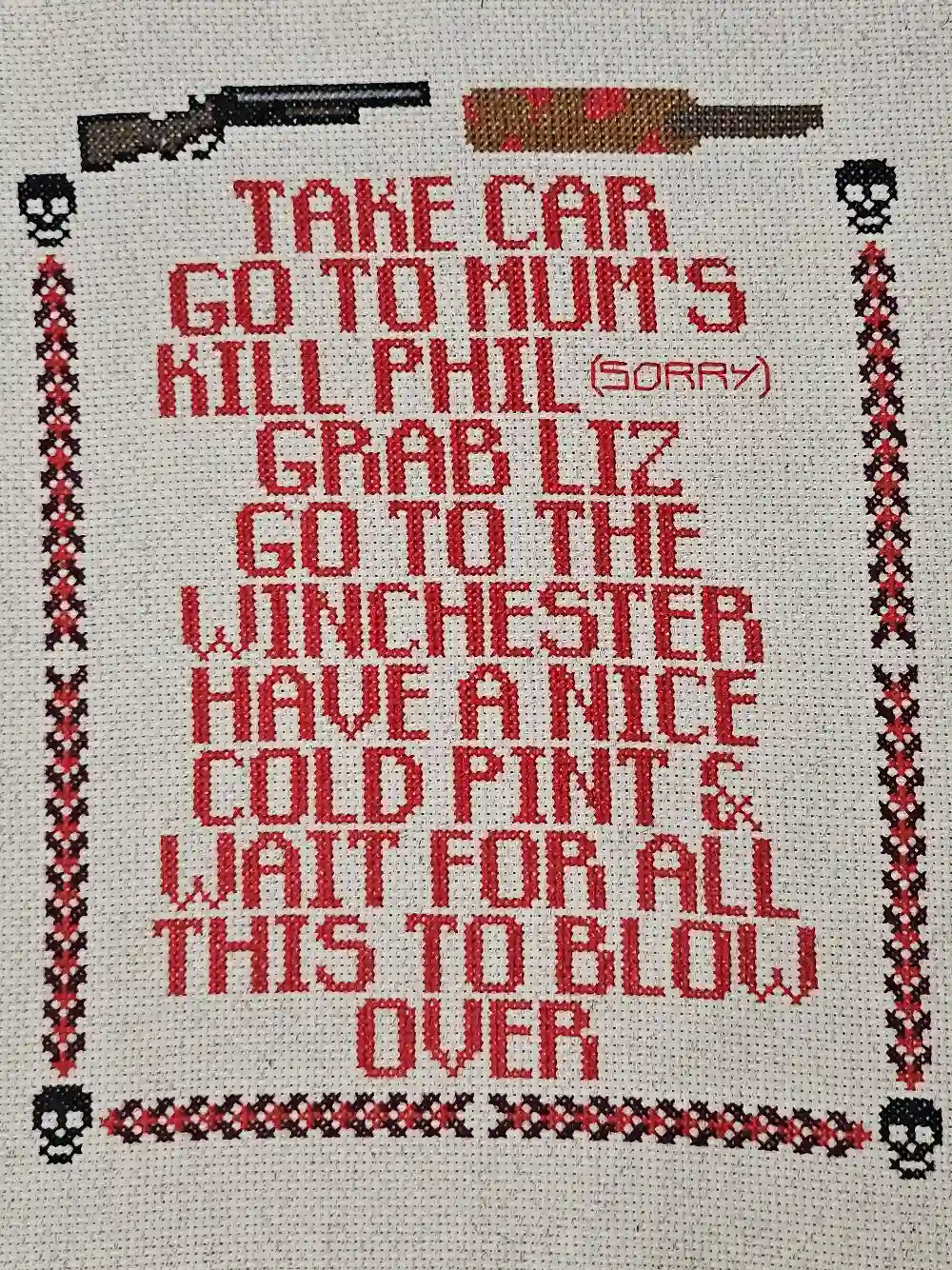 Red text reads: Take car, go to Mum's, kill Phil (sorry), grab Liz, go to the Winchester, have a nice cold pint & wait for all this to blow over. It's framed by skulls, a rifle, and a cricket bat. Cross-stitch.