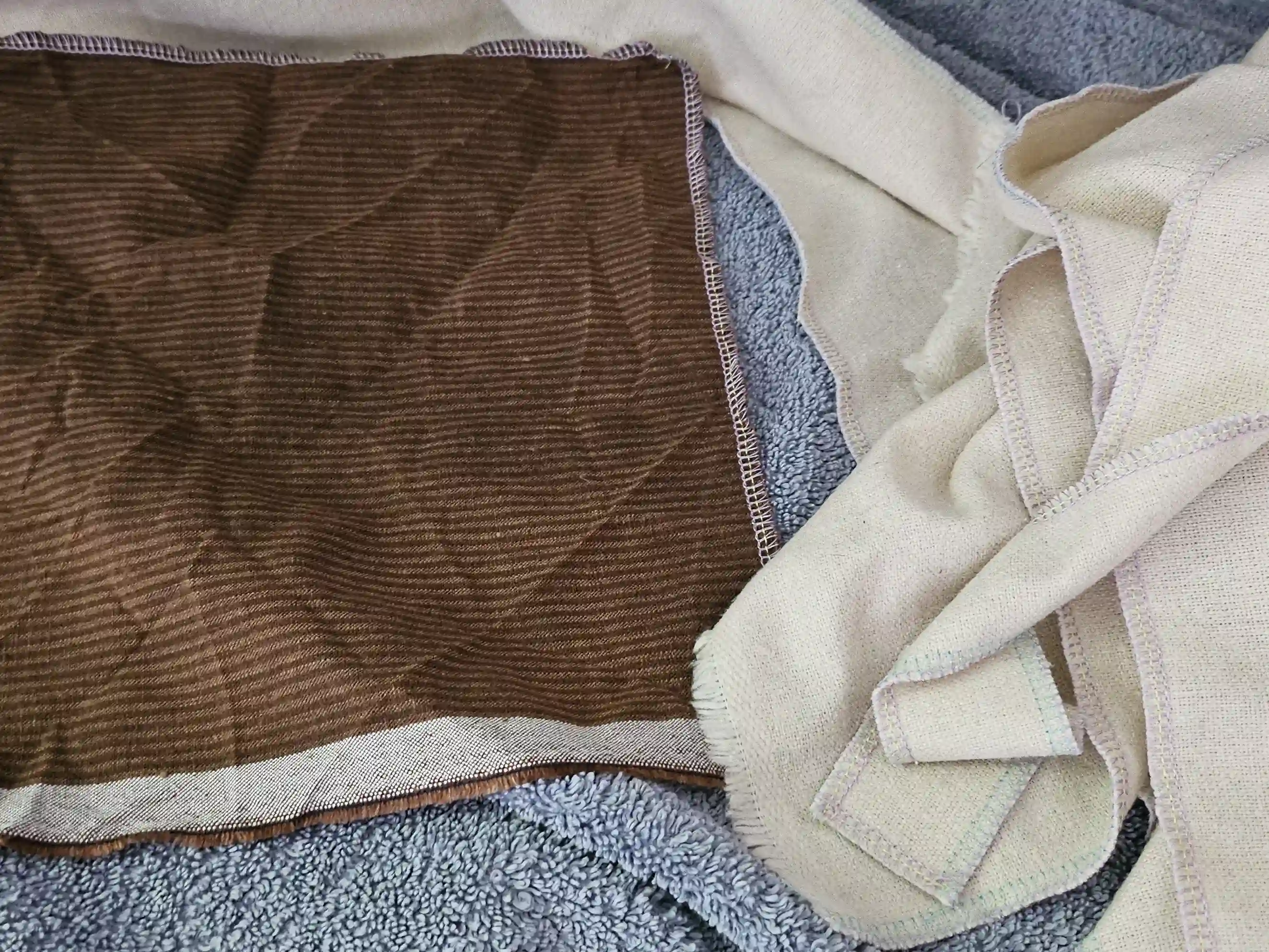 A brown striped linen and cream colored linen lay over a blue towel.