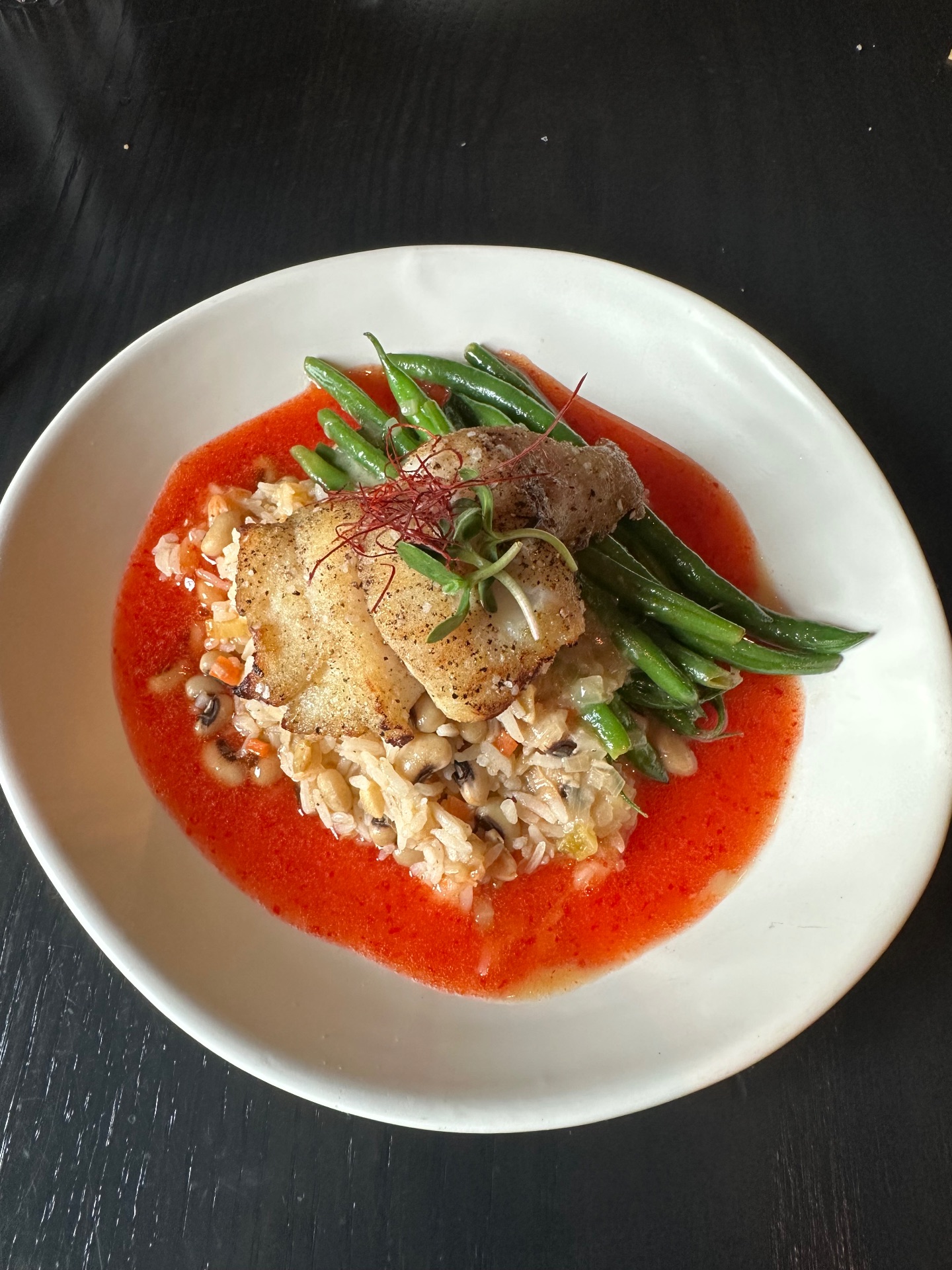 Grouper on hoppin john with haricot vert surrounded by a bright red sauce.