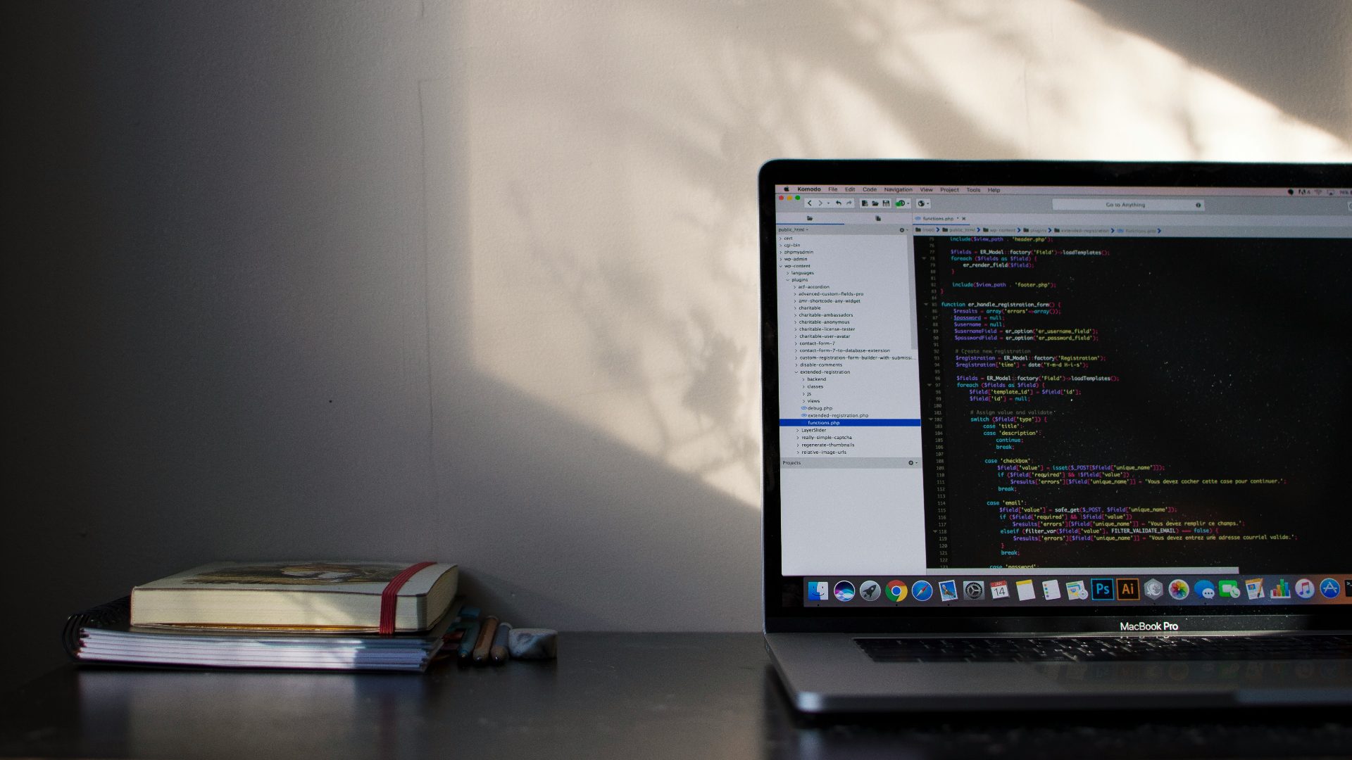 desk with a book and a notebook and a laptop opened in a code editor