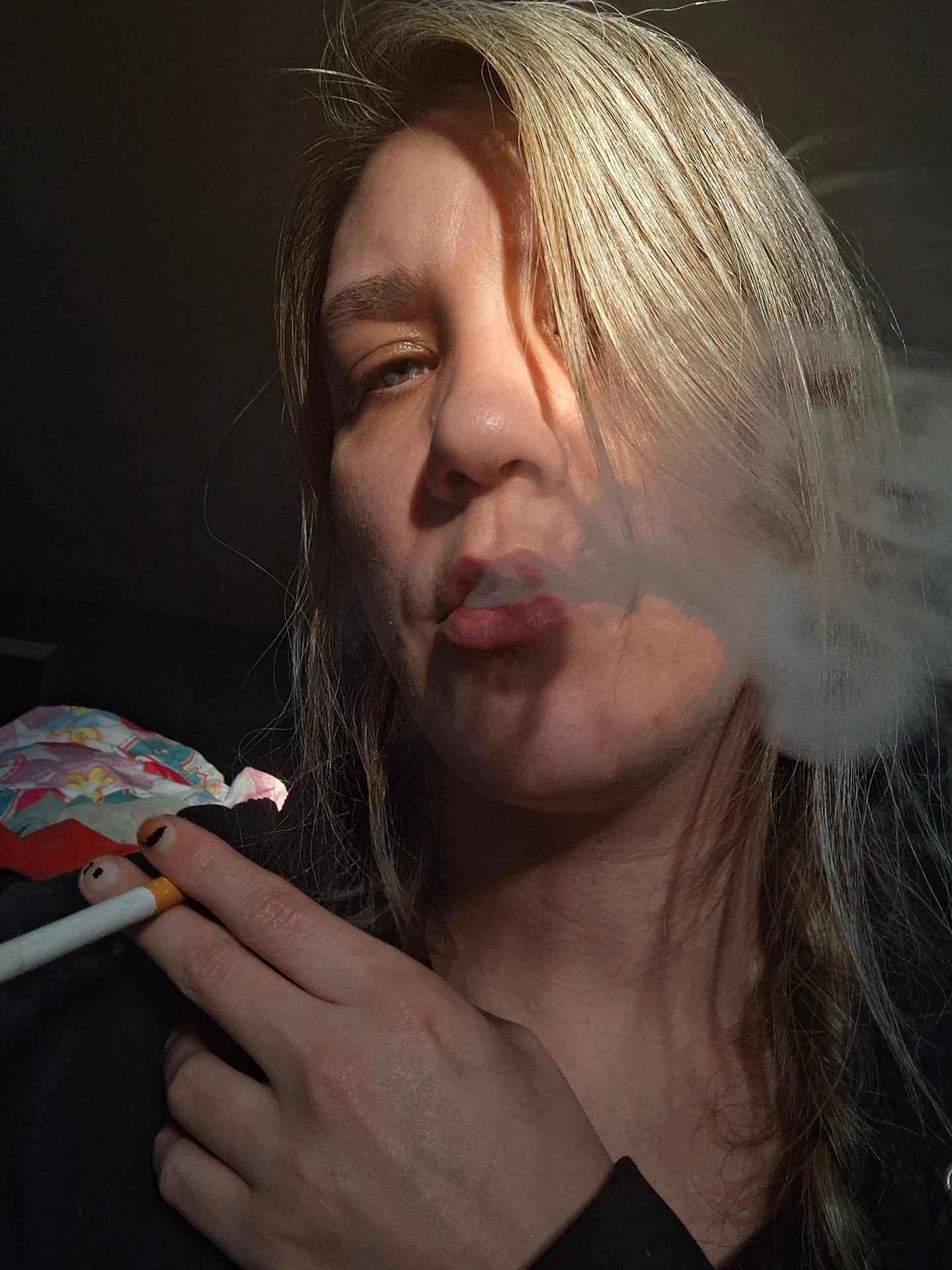 Valerie Rayne exhales a cork-filtered cigarette eith the sunlight slightly on her face.