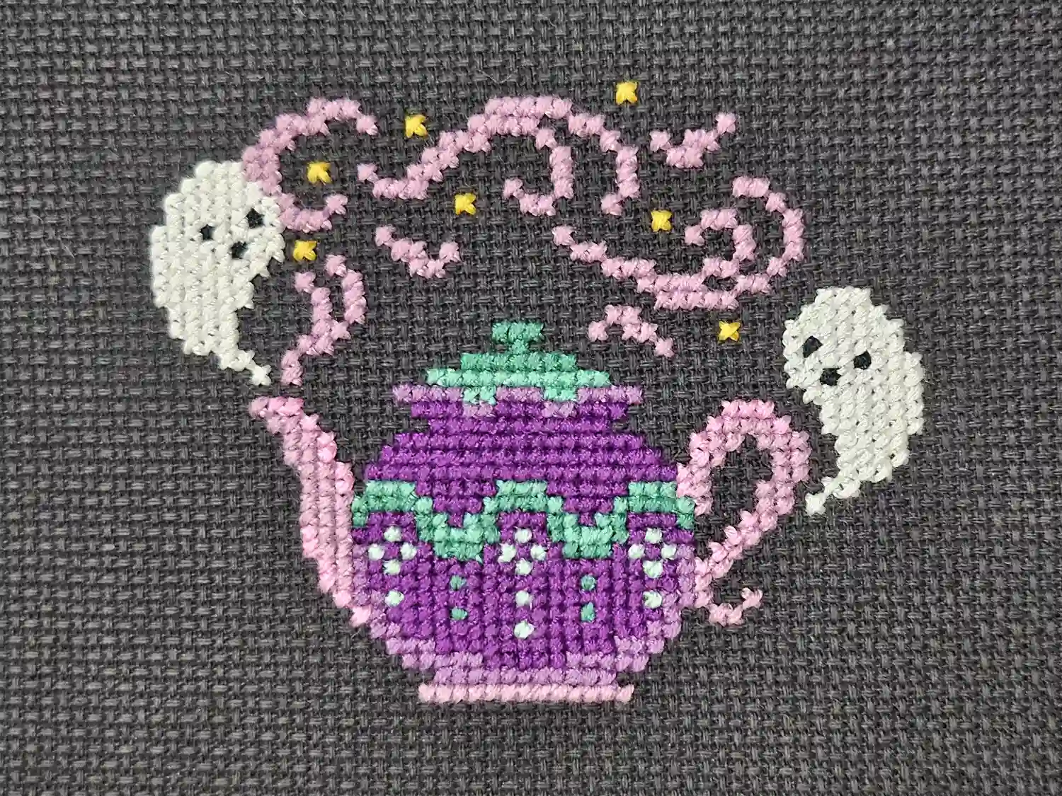 Two ghosts swirl around a purple teapot. Cross-stitch.