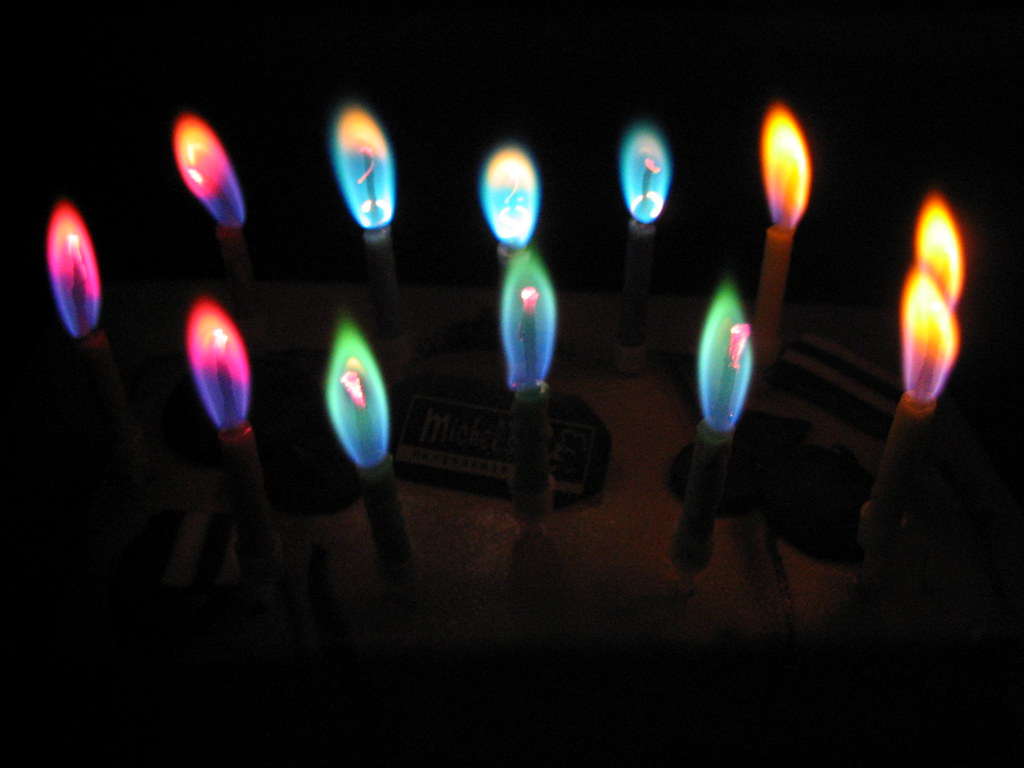 12 birthday candles lit in an oval shape, they're the kind of candles that burn different color flames so there are pink ones, green ones, blue ones and yellow ones. it's very dark in the room