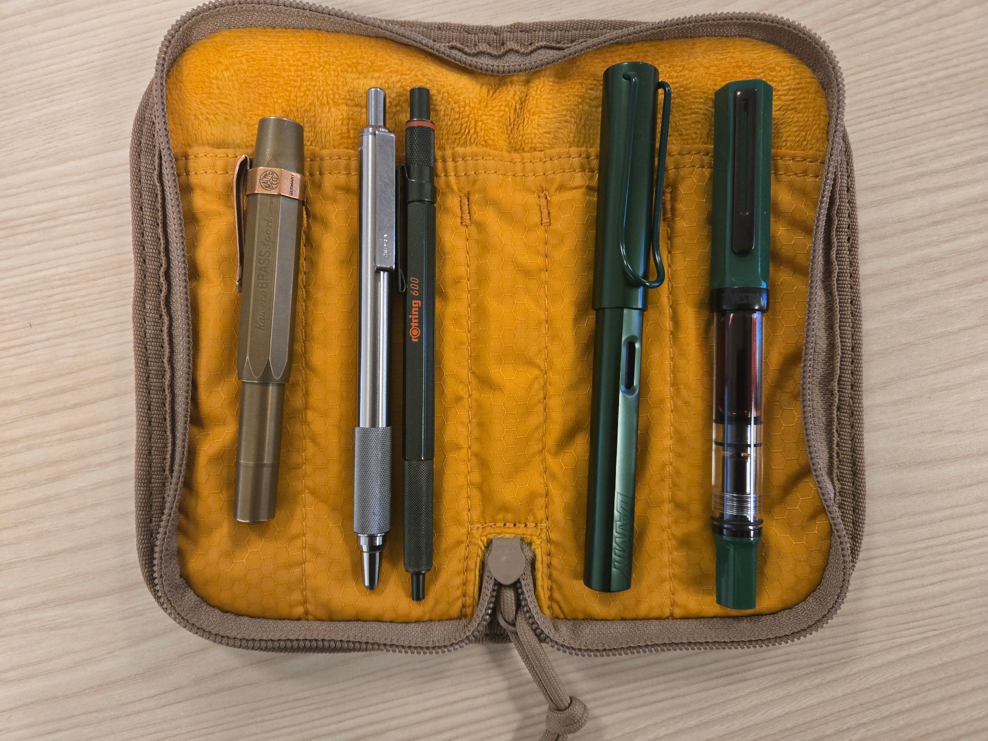 Pens lined up inside of a lochby quattro v2 case: (L to R) Kaweco Brass Sport, Zebra F-701, green rOtring 600, pine Lamy Al-Star, Irish Green TWSBI Eco