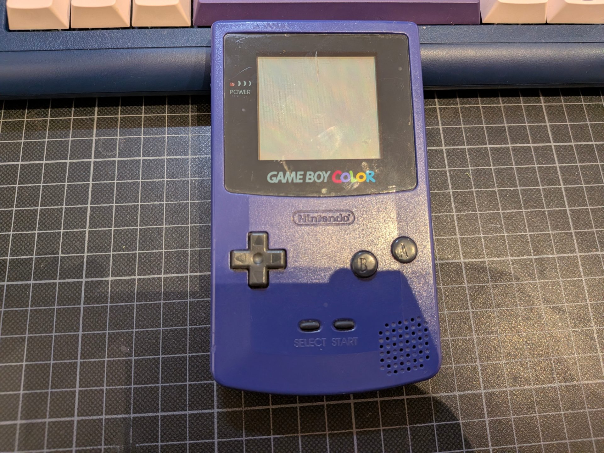 A purple gameboy color propped up on a keyboard for a better view.