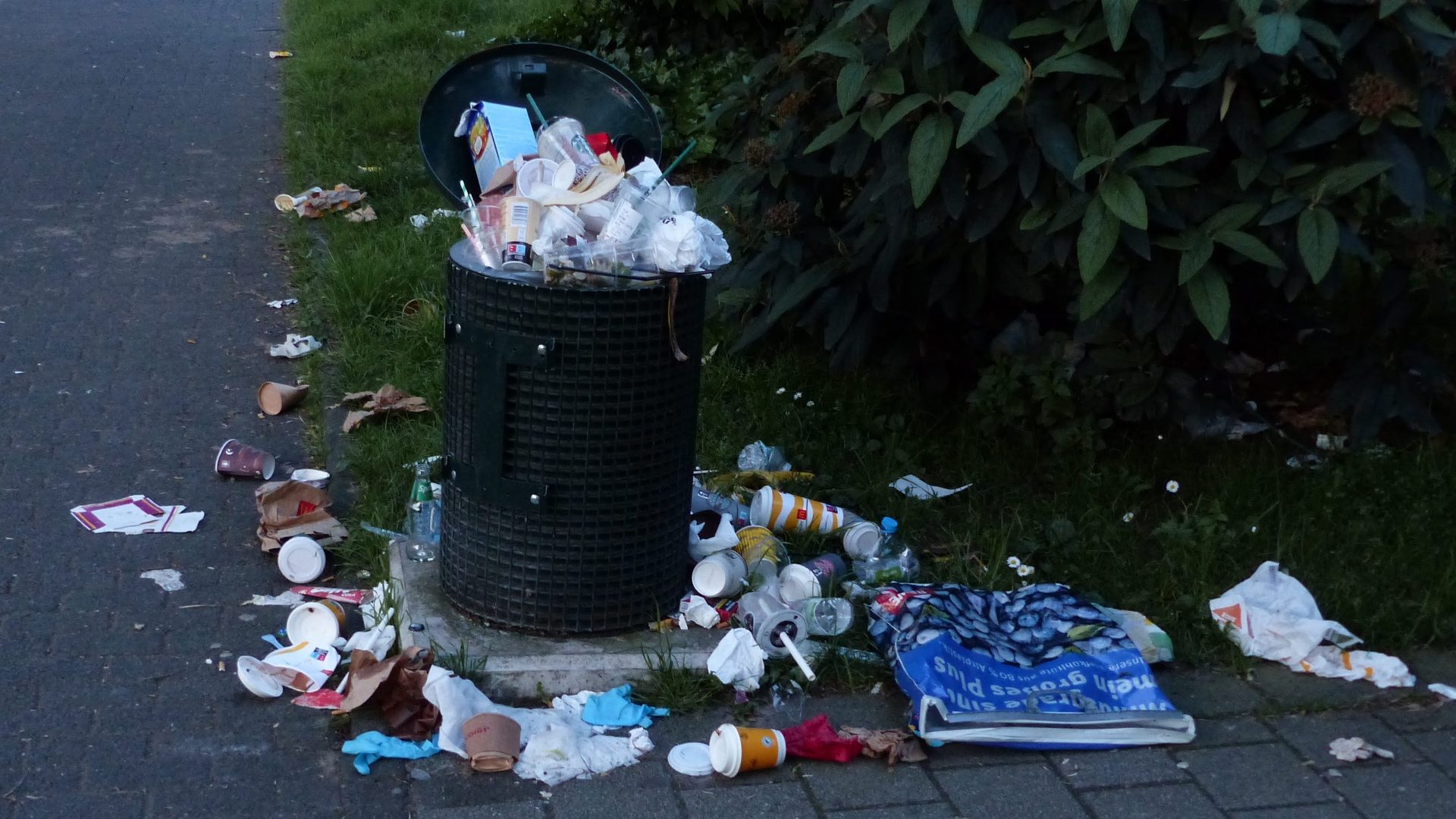 Überquillender Mülleimer und verschiedene Abfälle auf dem Fußboden davor.