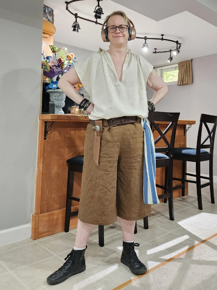 A white guy dressed in a pirate costume made of a white linen shirt and striped linen shorts.