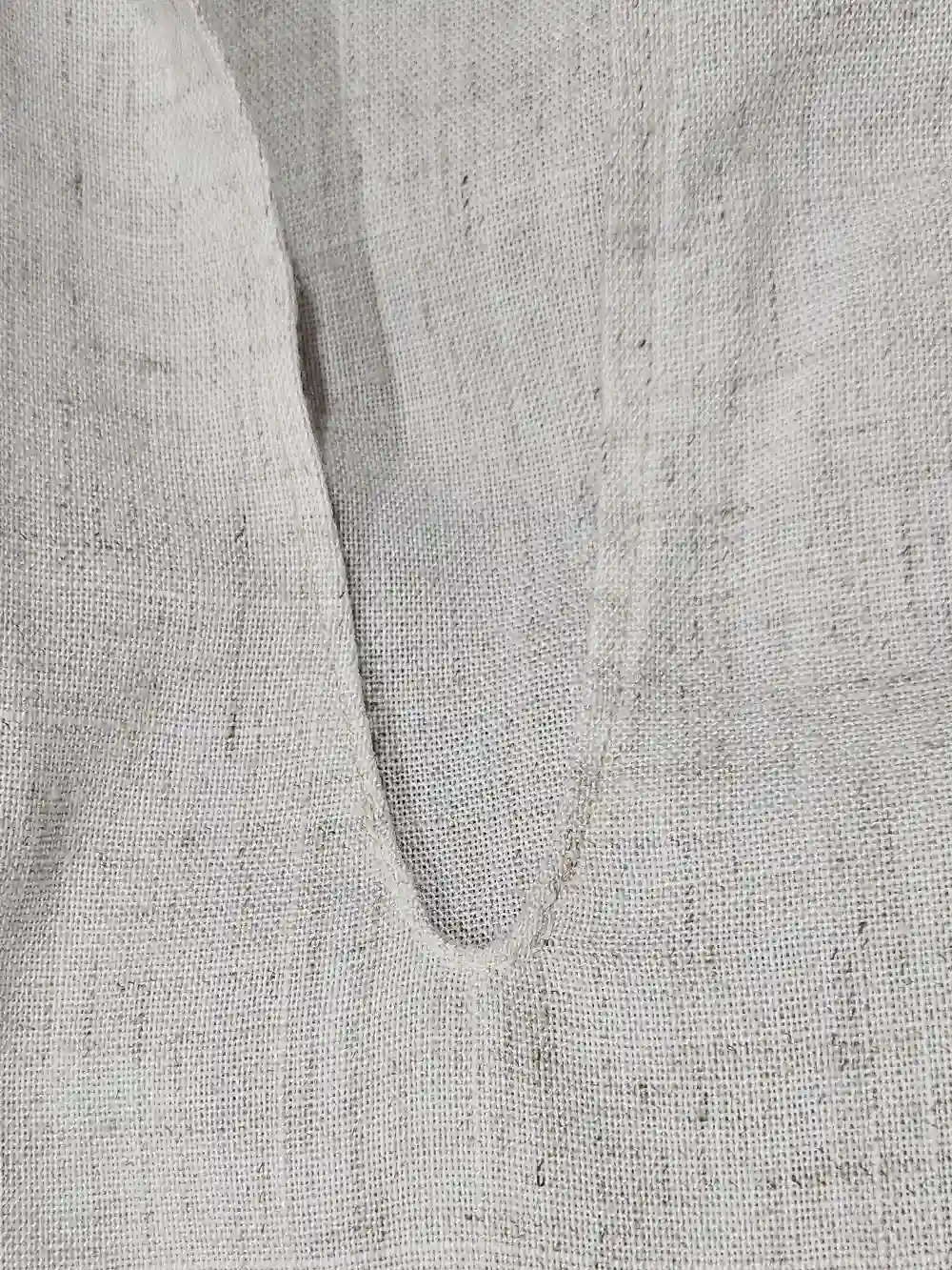 A collar of the linen shirt, showing small hand stitches at the deepest part of the v.